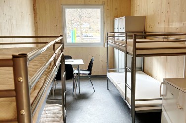 Blick in einen Wohncontainer, man sieht zwei Stockbetten, Schränke, Tisch und Stühle