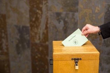Eine Frau steckt einen Wahlumschlag in eine Urne